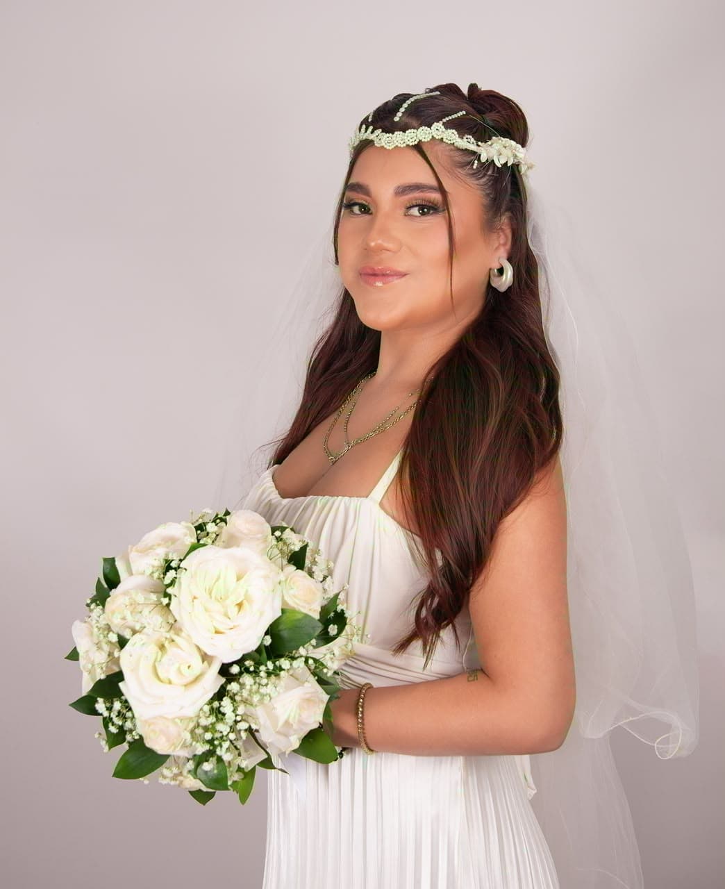 Maquillaje de novia con acabado natural luminoso, tonos nude y ojos difuminados, con velo, corona de flores y ramo de rosas blancas